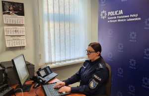 na zdjęciu widać siedzącą za biurkiem policjantkę, która prowadzi zajęcia on-line przed komputerem