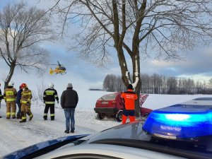 zdjęcie przedstawia volkswagena golfa, który uderzył w drzewo, nad nim leci helikopter