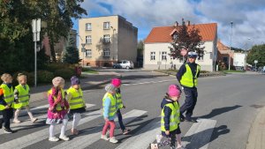 policjant przechodzi przez przejście dla pieszych wraz z dziećmi ubranymi w kamizelki odblaskowe
