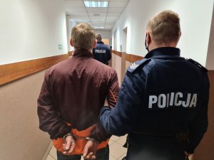 na zdjęciu widać mężczyznę, który ma założone kajdanki doprowadzanego przez policjantów do zakładu karnego
