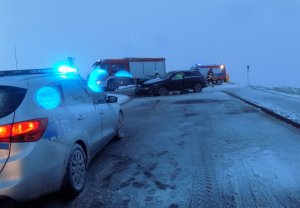 na zdjęciu widać policyjny radiowóz a w tle dwa rozbite auta, wokół jest śnieg