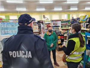 zdjęcie przedstawia policjanta i pracownika Powiatowej Stacji Sanitarno-Epidemiologicznej podczas rozmowy z pracownica sklepu