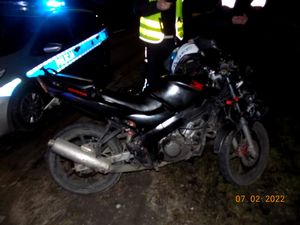 na zdjęciu widać motorower, który brał udział w kolizji, w tle oznakowany radiowóz policyjny i umundurowany policjant