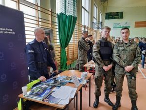 na zdjęciu widać policjanta z młodzieżą szkolną przy stoisku policyjnym
