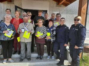 na pamiątkowym zdjęciu widać seniorów trzymających elementy odblaskowe wraz z dwiema policjantkami stojących na schodach przed Klubem Seniora