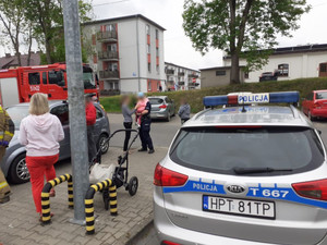 na zdjęciu widać policyjny radiowóz w tle dzielnicowa trzymająca dziecko na rękach