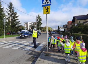 na zdjęciu widać policjanta ruchu drogowego pokazującego dzieciom jak prawidłowo przechodzić przez przejście dla pieszych