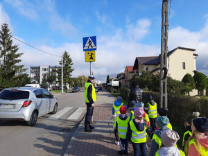 policjant pokazuje dzieciom znak drogowy przejście dla pieszych