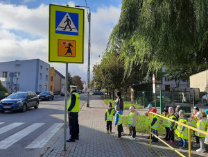 policjant pokazuje dzieciom jak prawidłowo przechodzić przez przejście dla pieszych