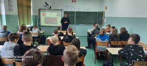na zdjęciu widać dzielnicowego rozmawiającego z uczniami w klasie